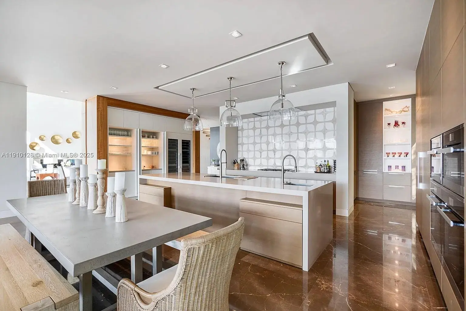 Modern kitchen with marble floors, large island, pendant lights, and a dining table with wicker chairs.