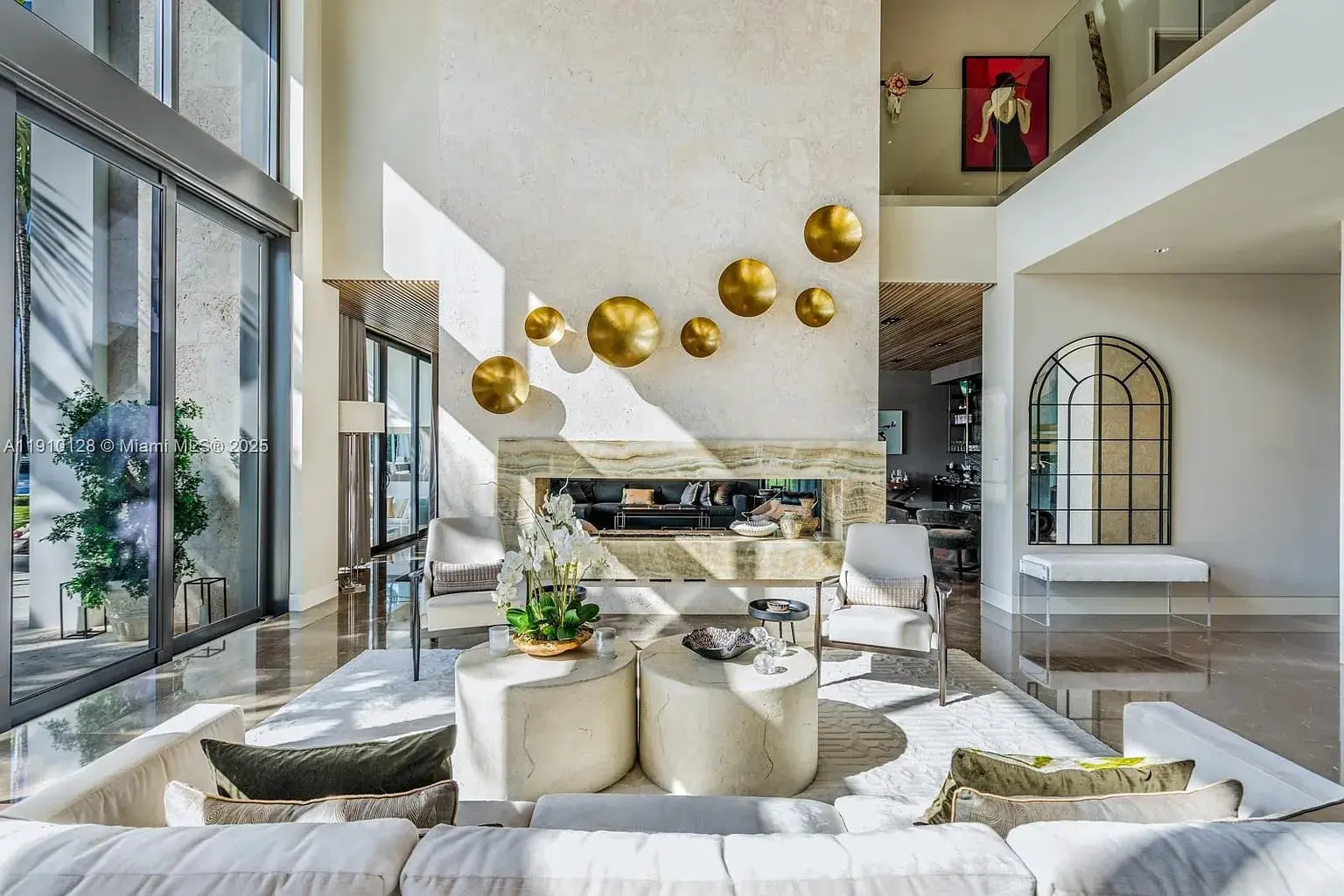 Spacious modern living room with large windows, gold wall decorations, and neutral-toned furniture.