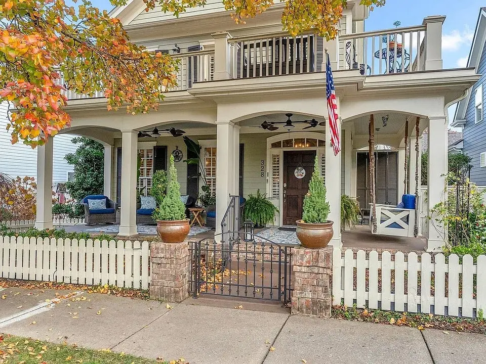 Charming two-story house with a porch, autumn leaves, and American flag in front yard.