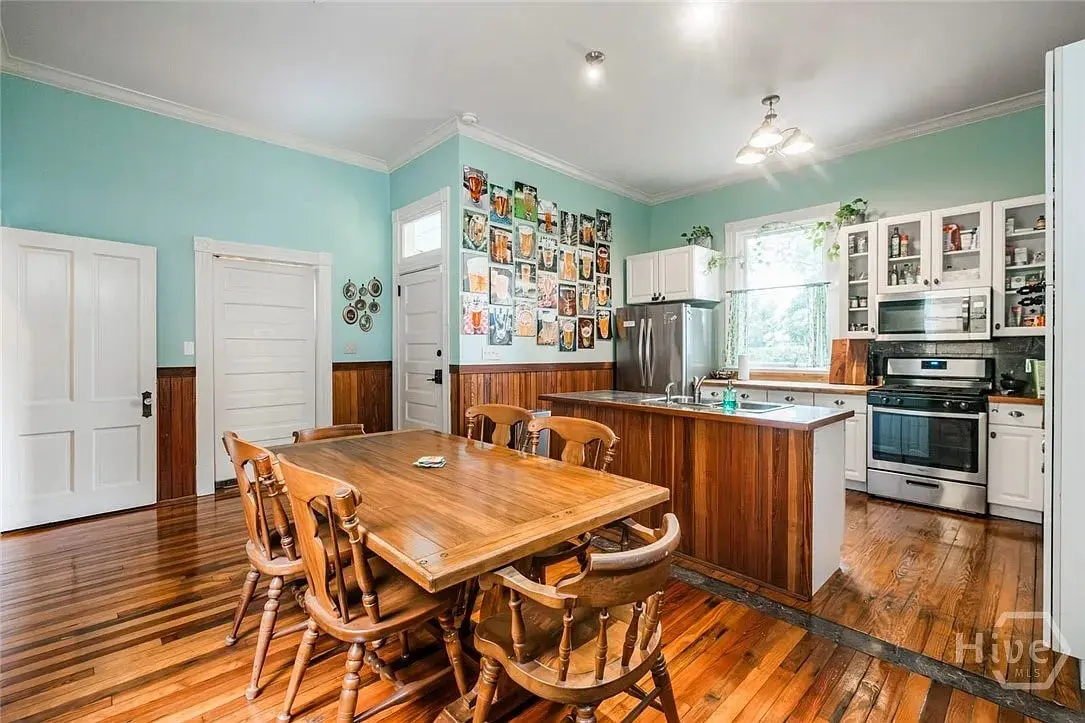 Spacious kitchen with wooden dining table, teal walls, and a collage of photos on one wall.