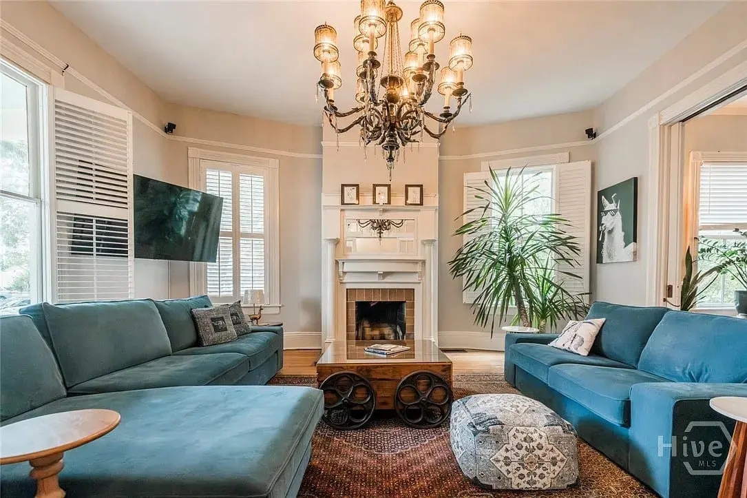 Living room with blue sofas, a chandelier, fireplace, large plants, and a wall-mounted TV.