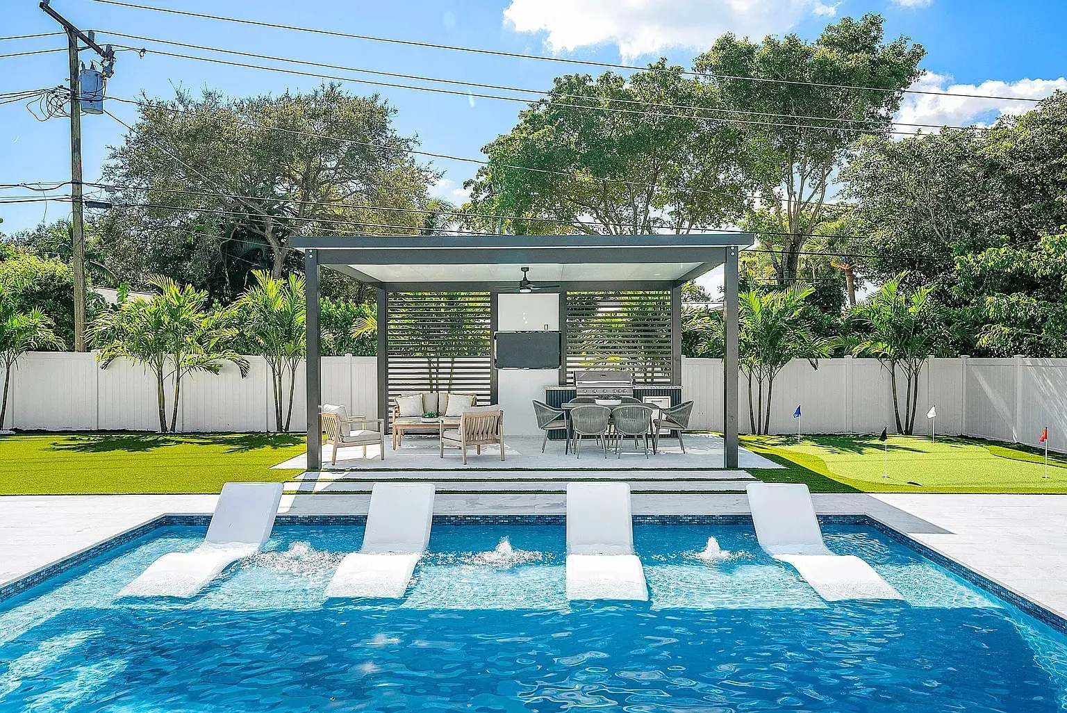 Modern backyard with a pool, submerged lounge chairs, and a shaded seating area under a pergola.