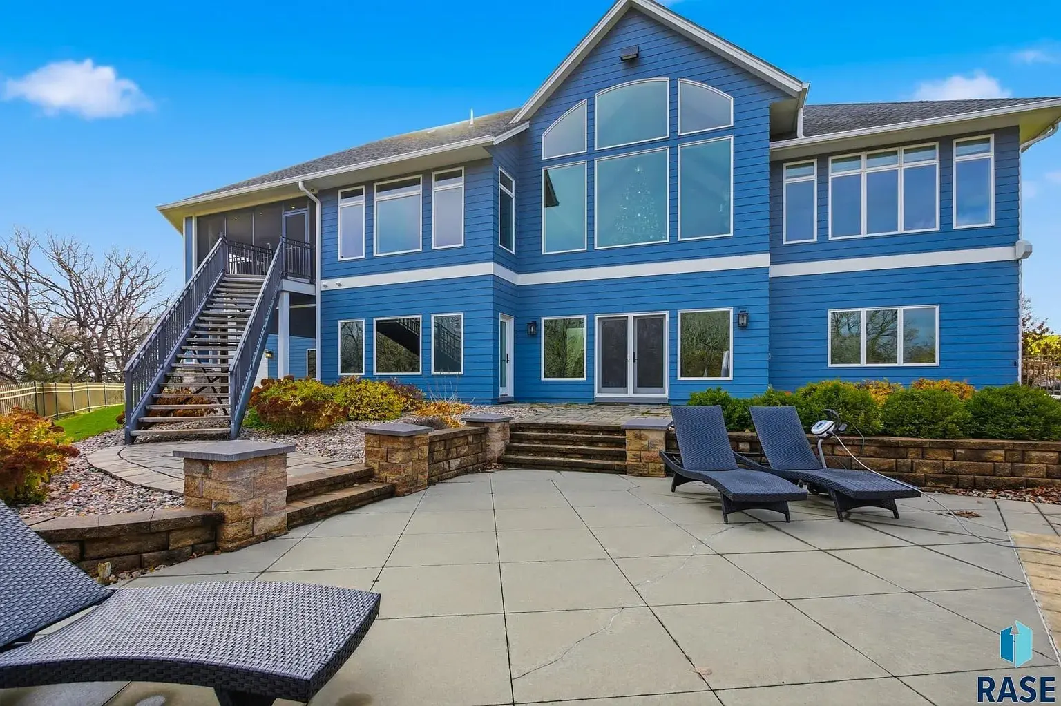 Blue two-story house with large windows, outdoor patio, and lounge chairs.