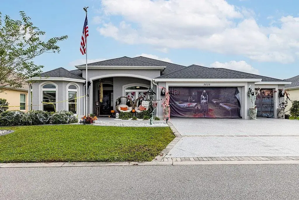 Single-story house with Halloween decorations and an American flag, featuring a large driveway.