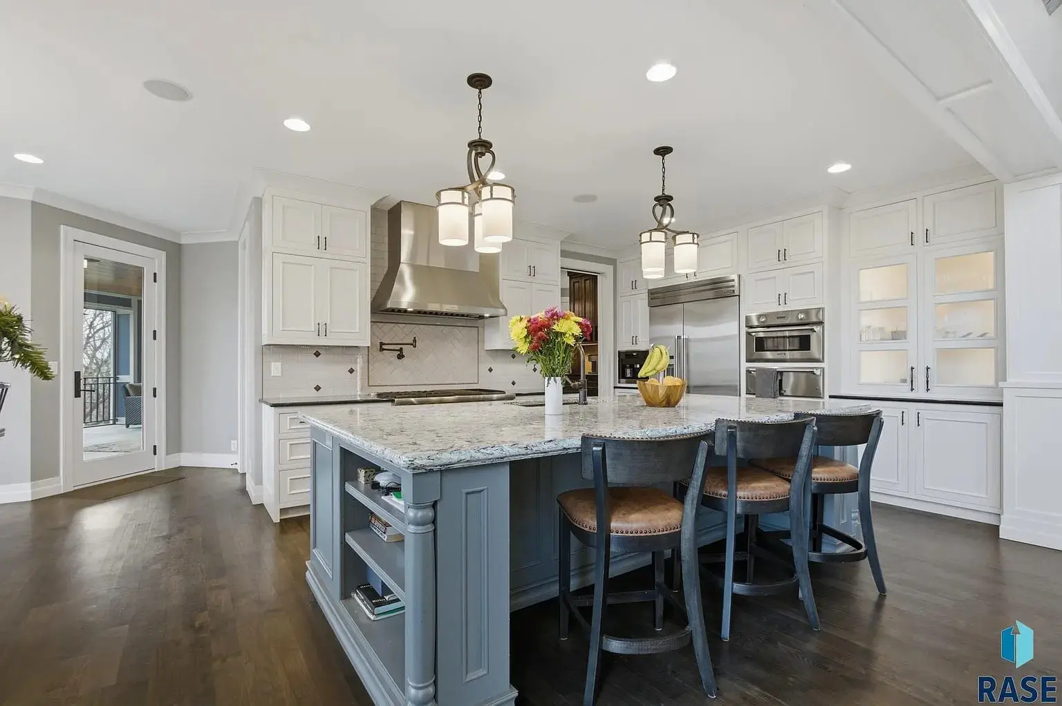 Modern kitchen with a large island, marble countertop, pendant lights, and stainless steel appliances.