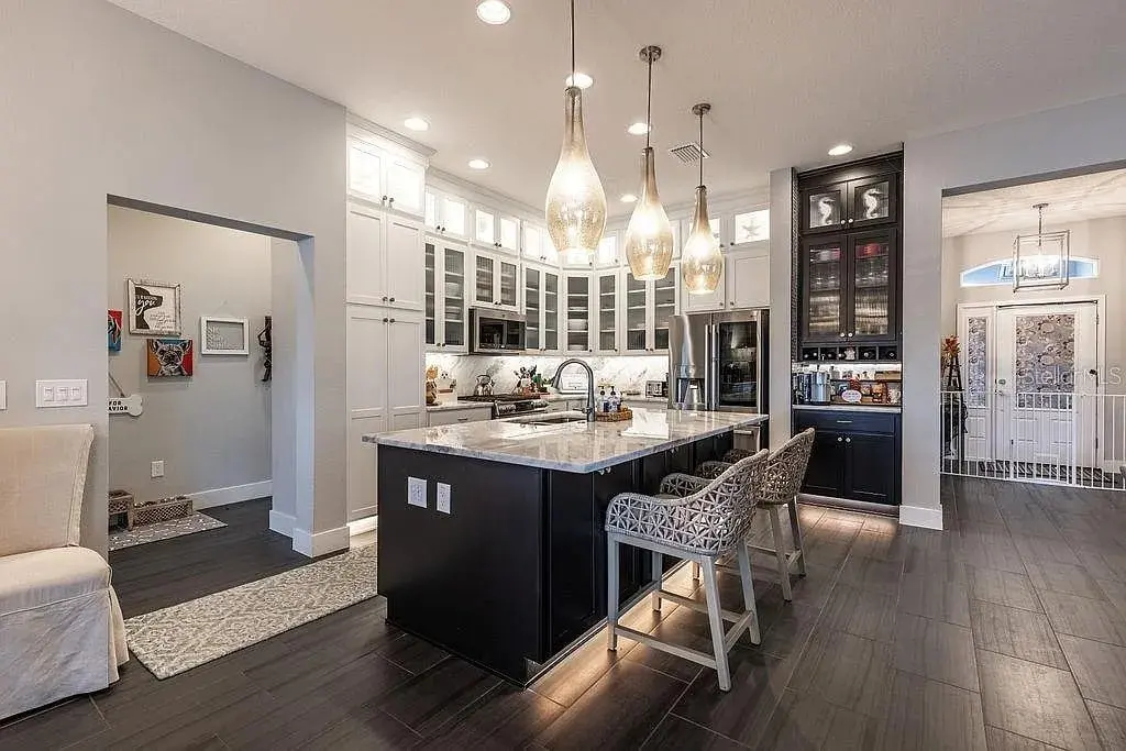 Modern kitchen with island, pendant lights, dark wood floors, and white cabinets.