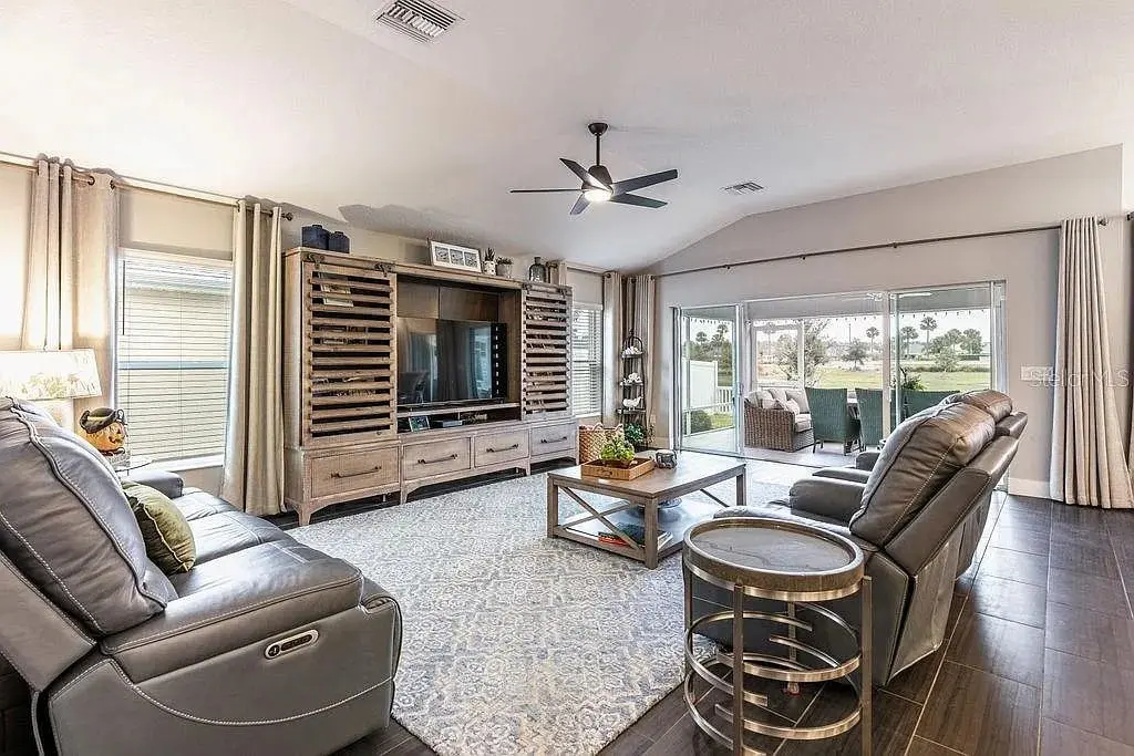 Spacious living room with leather sofas, large TV, ceiling fan, and sliding glass doors to patio.