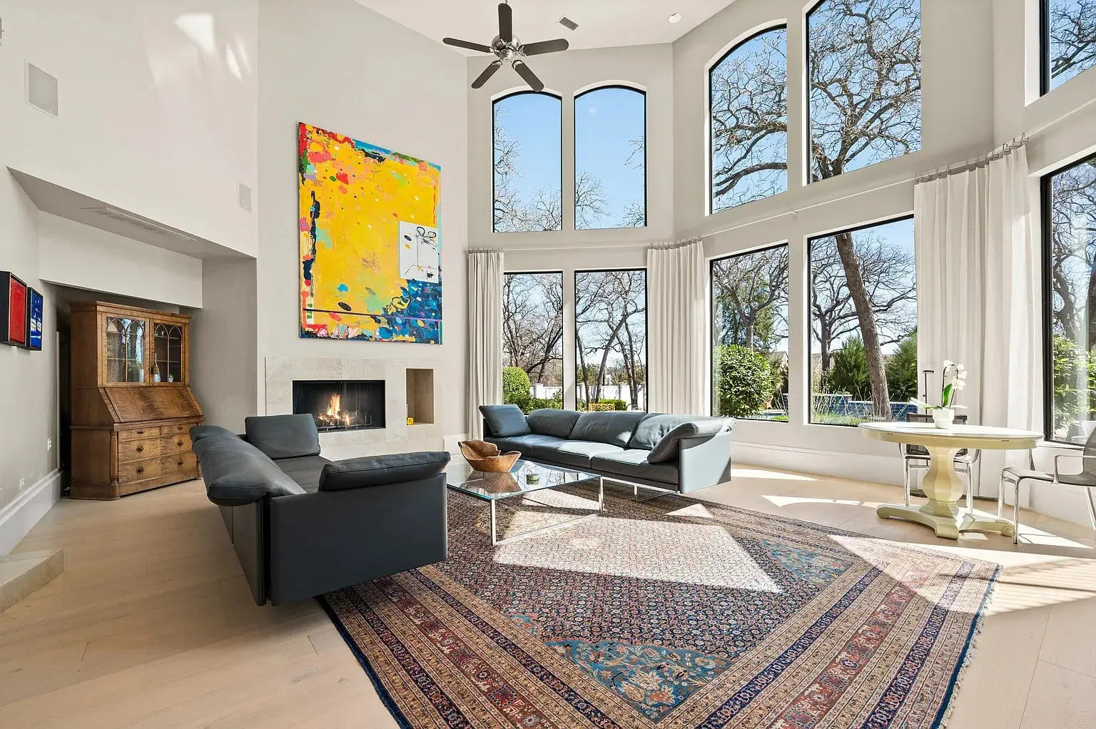 Spacious living room with large windows, modern furniture, colorful artwork, and a decorative rug.