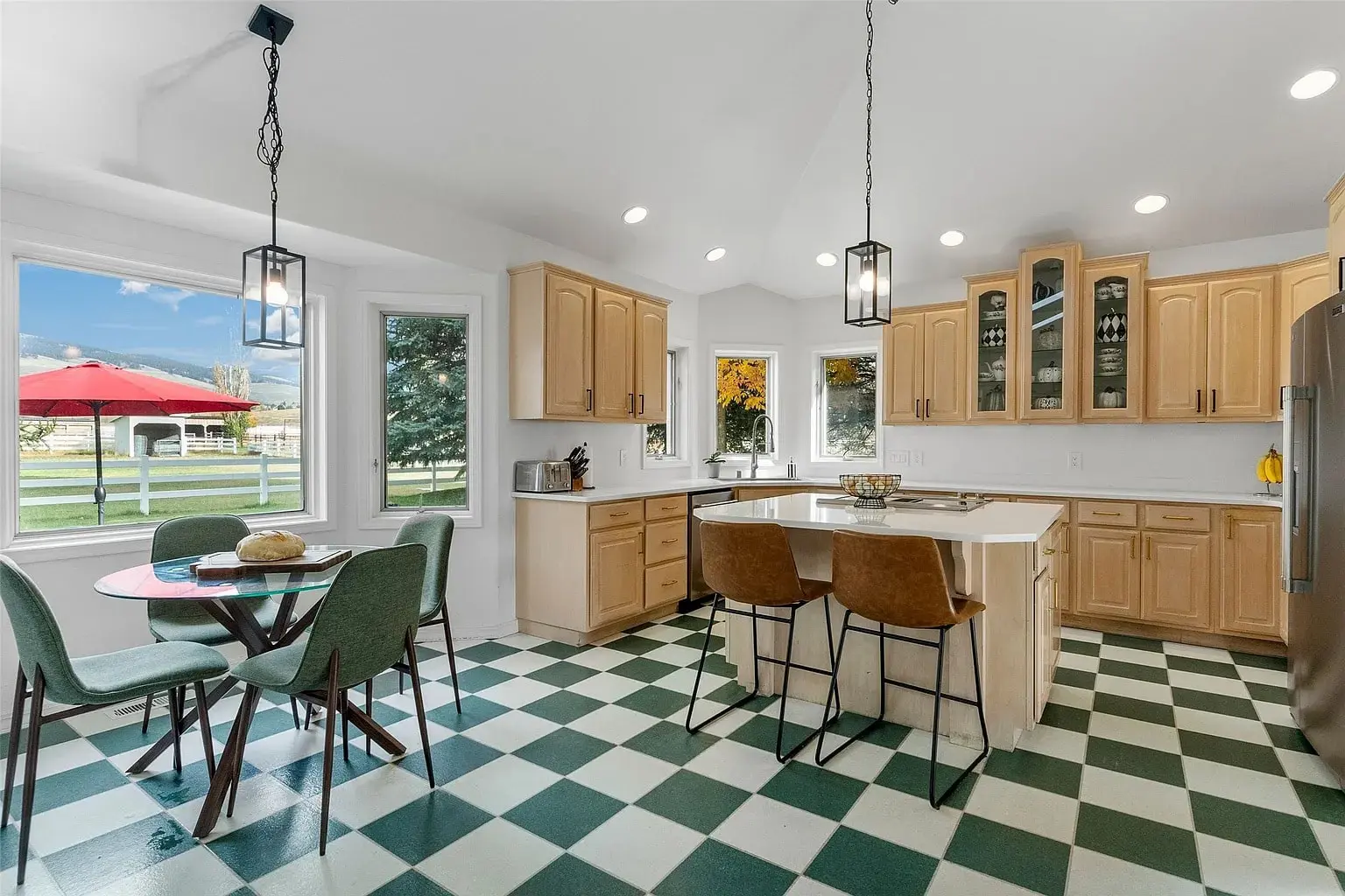 Spacious kitchen with checkered floor, wooden cabinets, island, and dining area with green chairs.