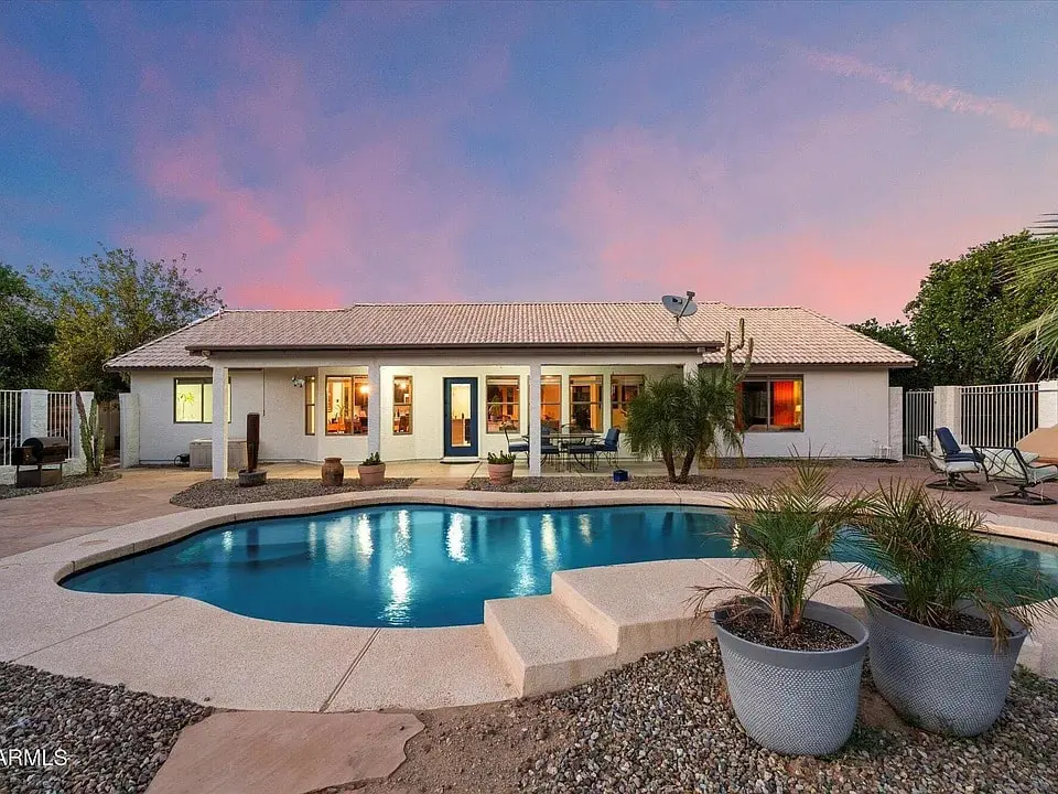 Backyard view of a house with a swimming pool, patio, and sunset sky.