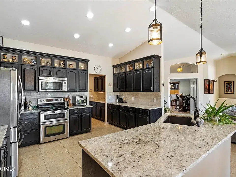 Modern kitchen with dark cabinets, stainless steel appliances, granite countertops, and pendant lighting.