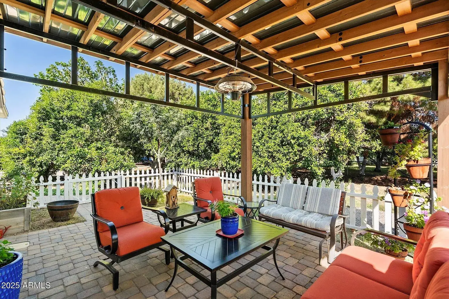 Covered patio with orange seating, a coffee table, and a white picket fence in the background.