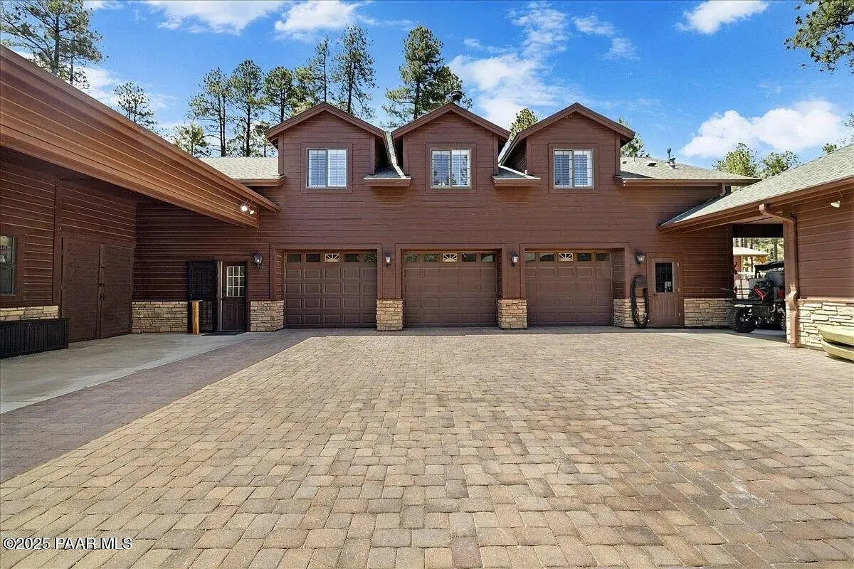 Large brown house with three garage doors and a spacious paved driveway.