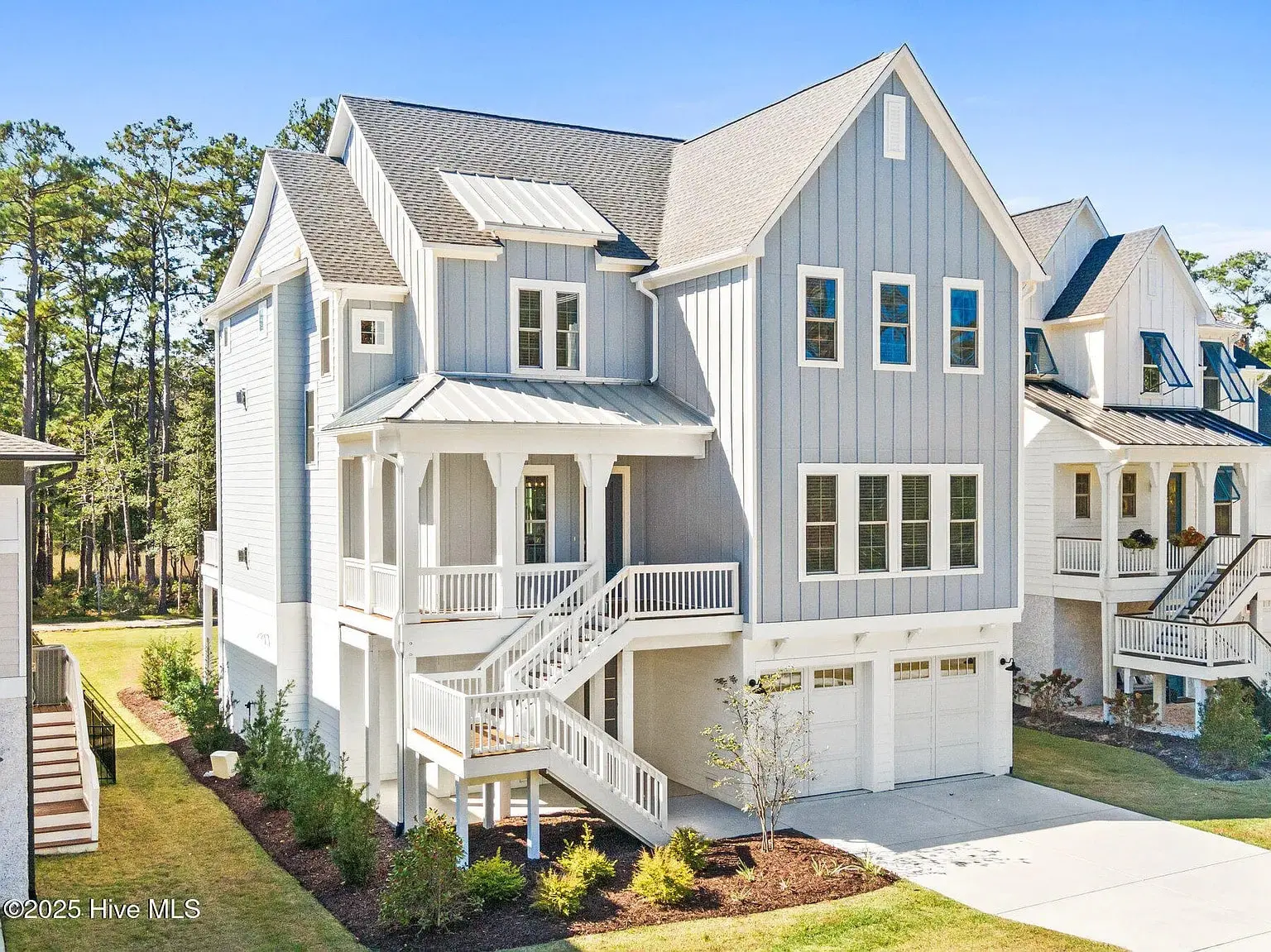 Modern two-story gray house with white trim, elevated porch, and double garage, surrounded by trees.