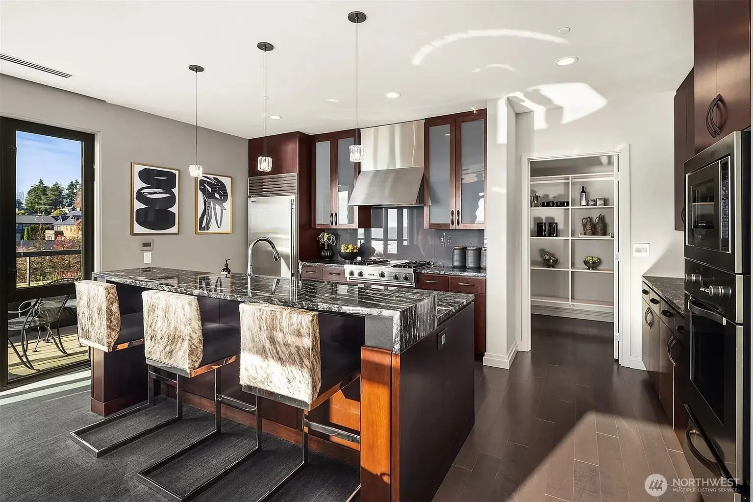 Modern kitchen with dark wood cabinets, marble island, stainless steel appliances, and fur-covered bar stools.