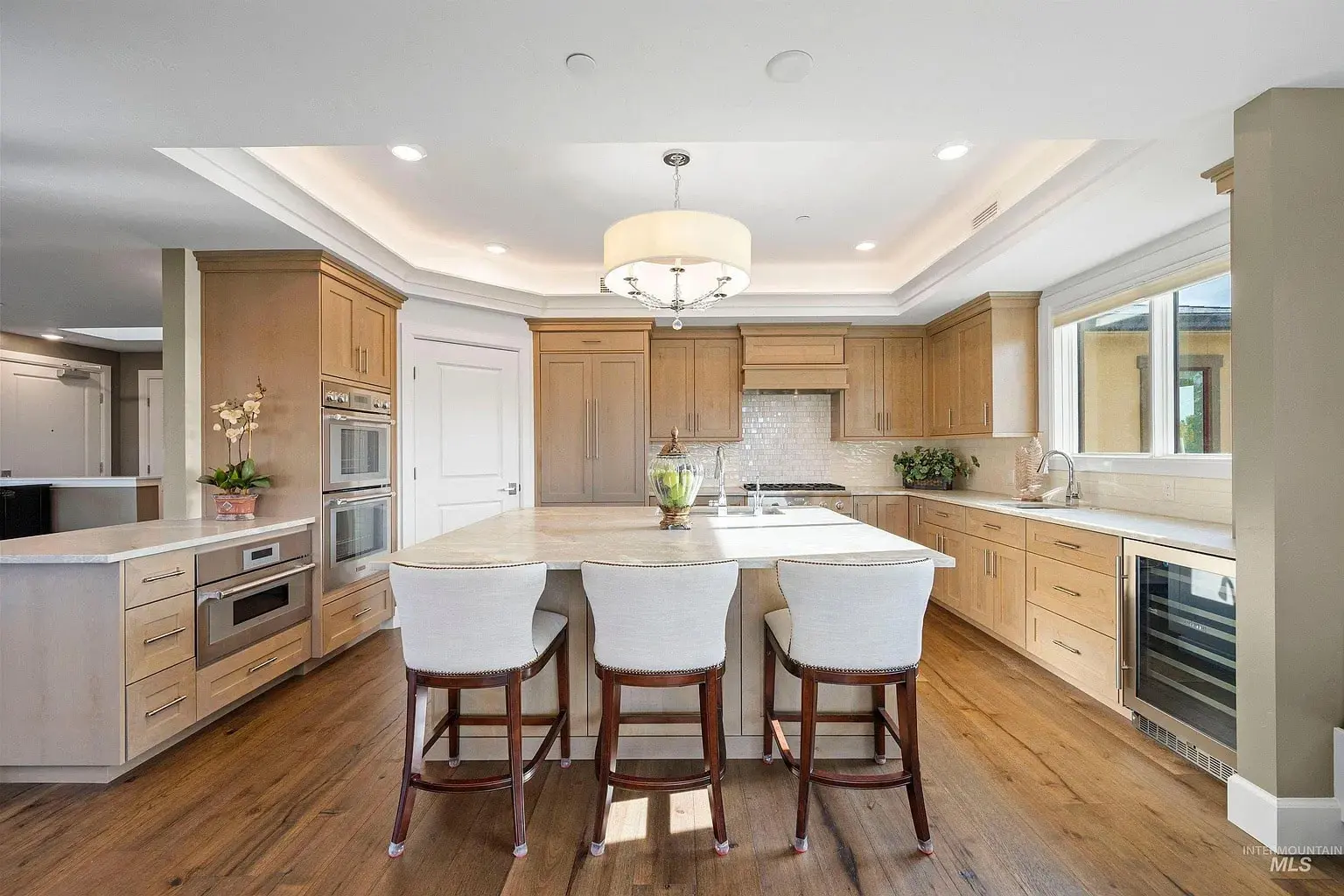 Modern kitchen with wooden cabinets, large island, three chairs, and stainless steel appliances.