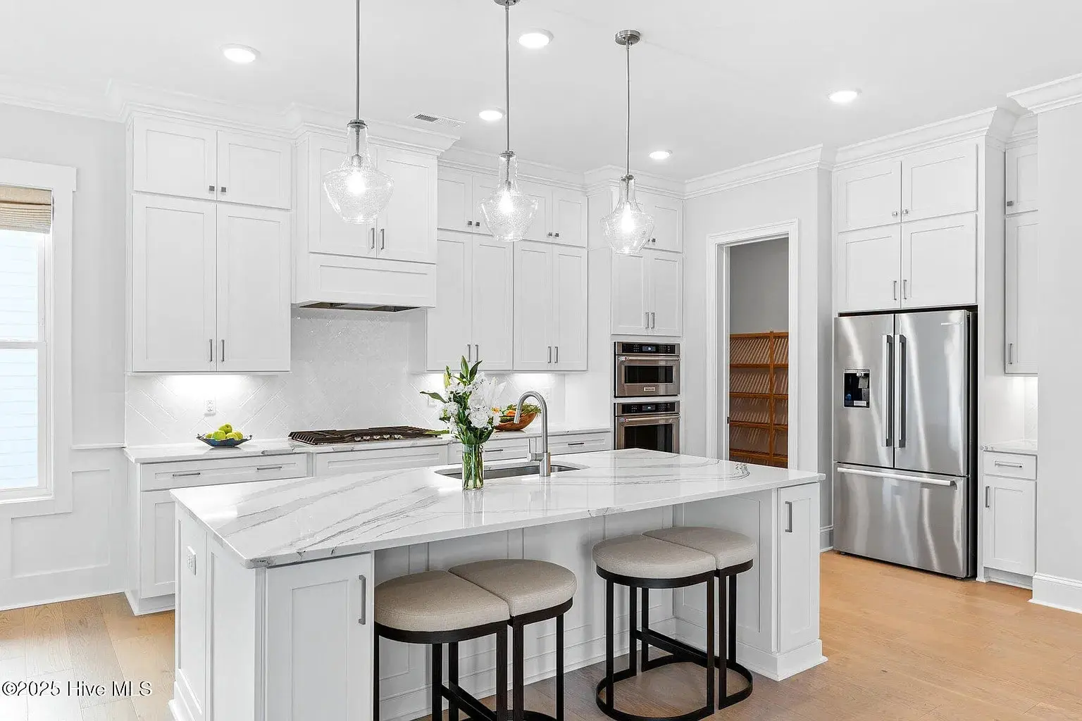 Modern kitchen with white cabinets, marble island, stainless steel appliances, and pendant lights.