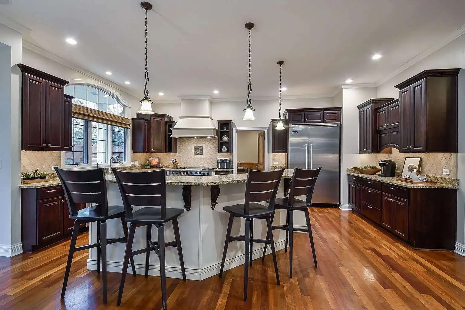 Spacious kitchen with dark wood cabinets, large island, stainless steel appliances, and hardwood floors.