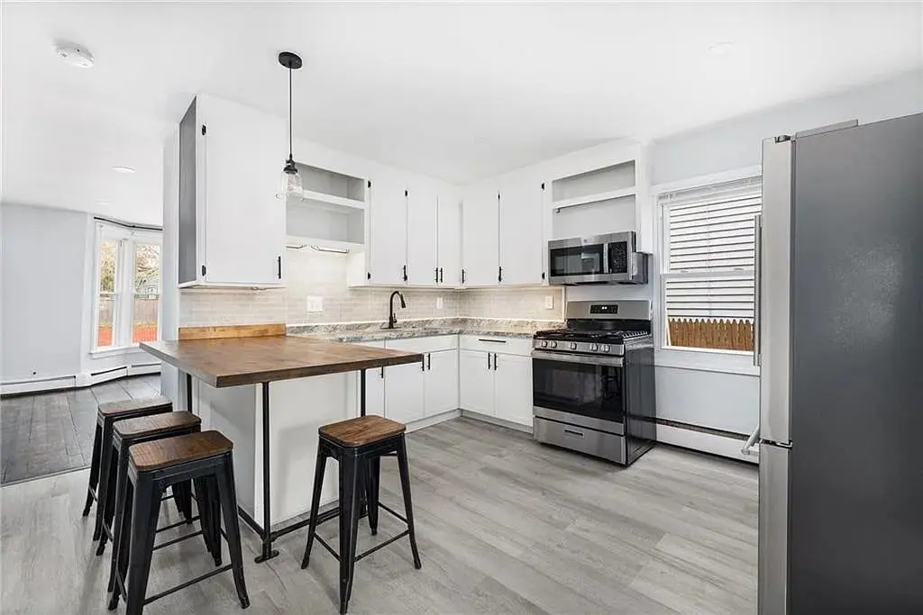 Modern kitchen with white cabinets, stainless steel appliances, wooden island, and bar stools.