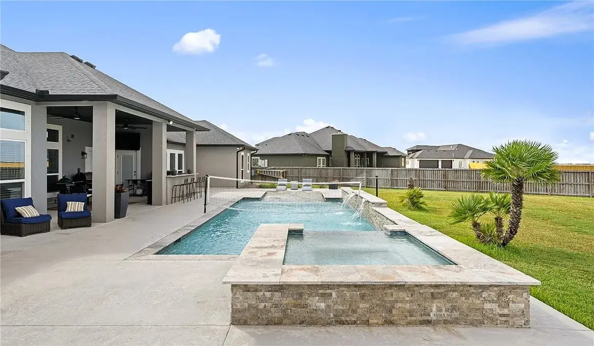 Modern backyard with a rectangular pool, spa, and patio furniture, surrounded by a wooden fence.