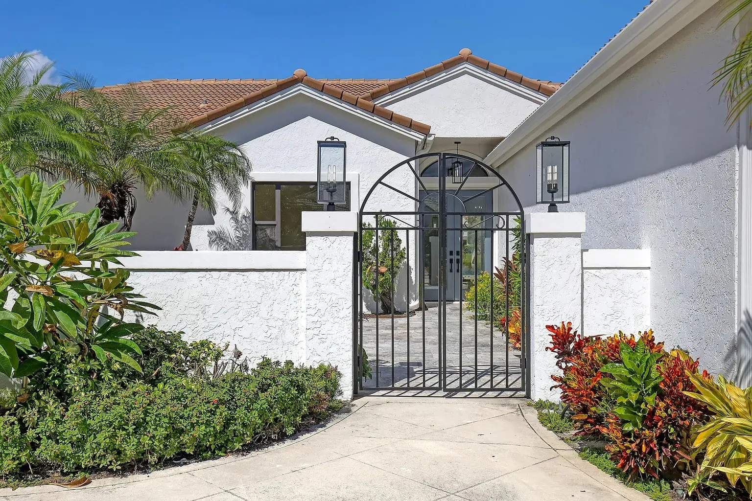 White house with a gated entrance, surrounded by tropical plants and a clear blue sky.