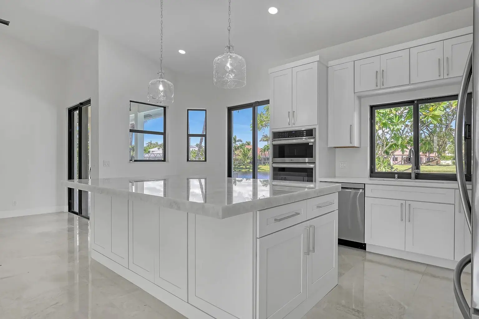 Modern kitchen with white cabinets, marble island, stainless steel appliances, and large windows.