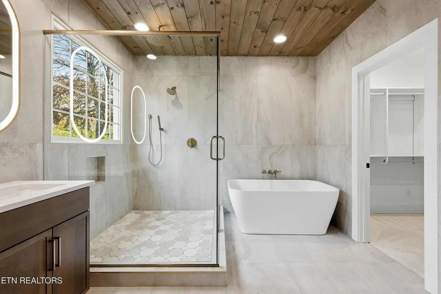 Modern bathroom with glass shower, freestanding bathtub, wood ceiling, and large window.