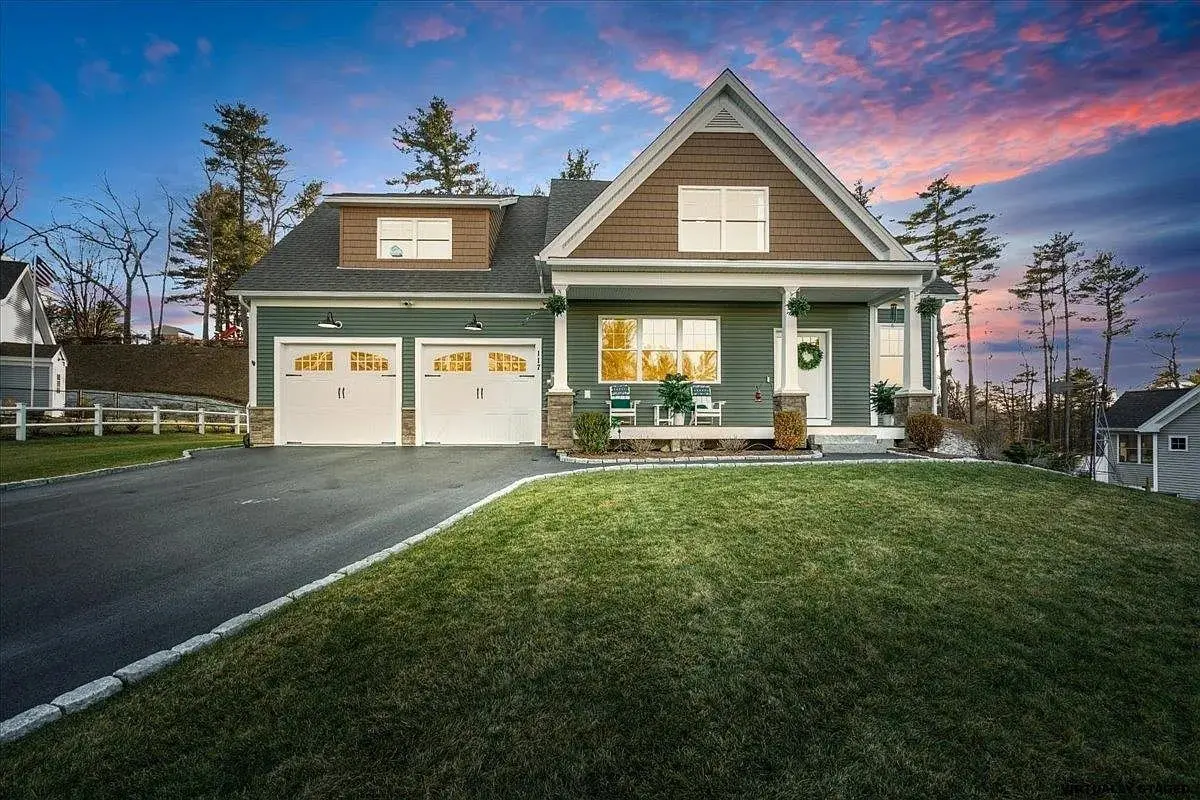 A two-story house with a double garage, front porch, and manicured lawn at sunset.