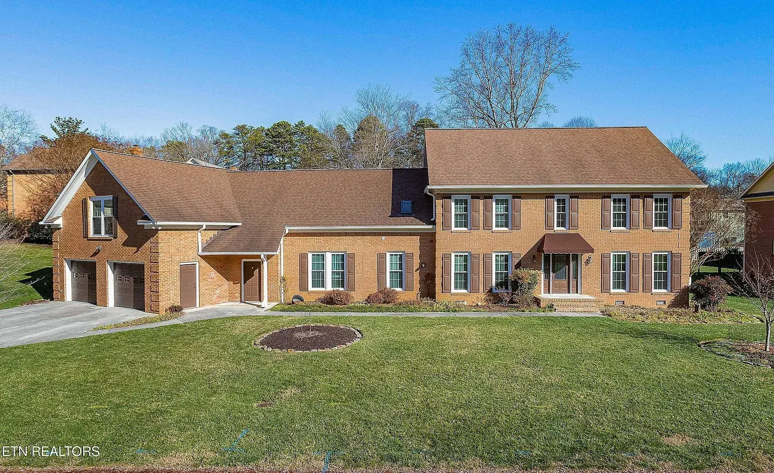 Large brick two-story home with attached two-car garage and well-kept lawn on a sunny day.
