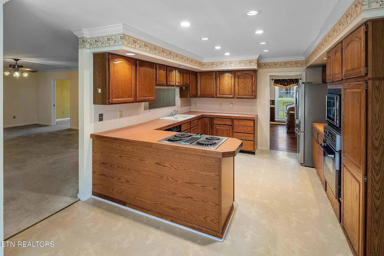 Spacious kitchen with oak cabinets, peninsula cooktop, recessed lights, stainless appliances, and openings to dining and living areas.