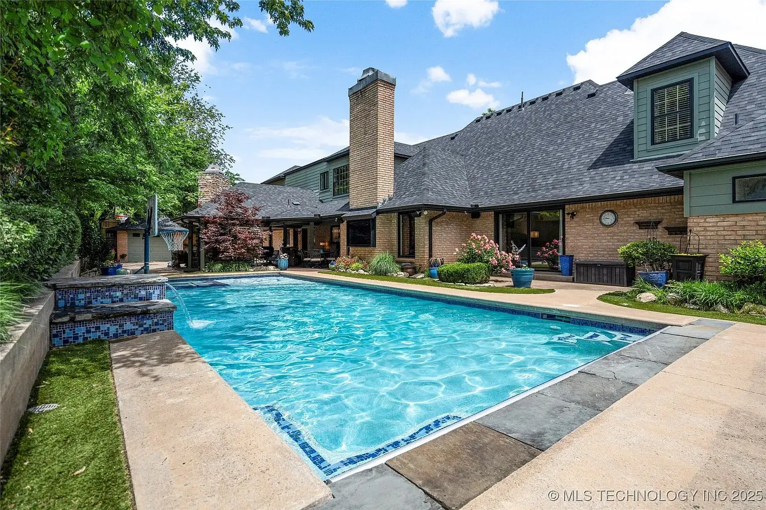 Backyard view of a house with a swimming pool, surrounded by greenery and potted plants.