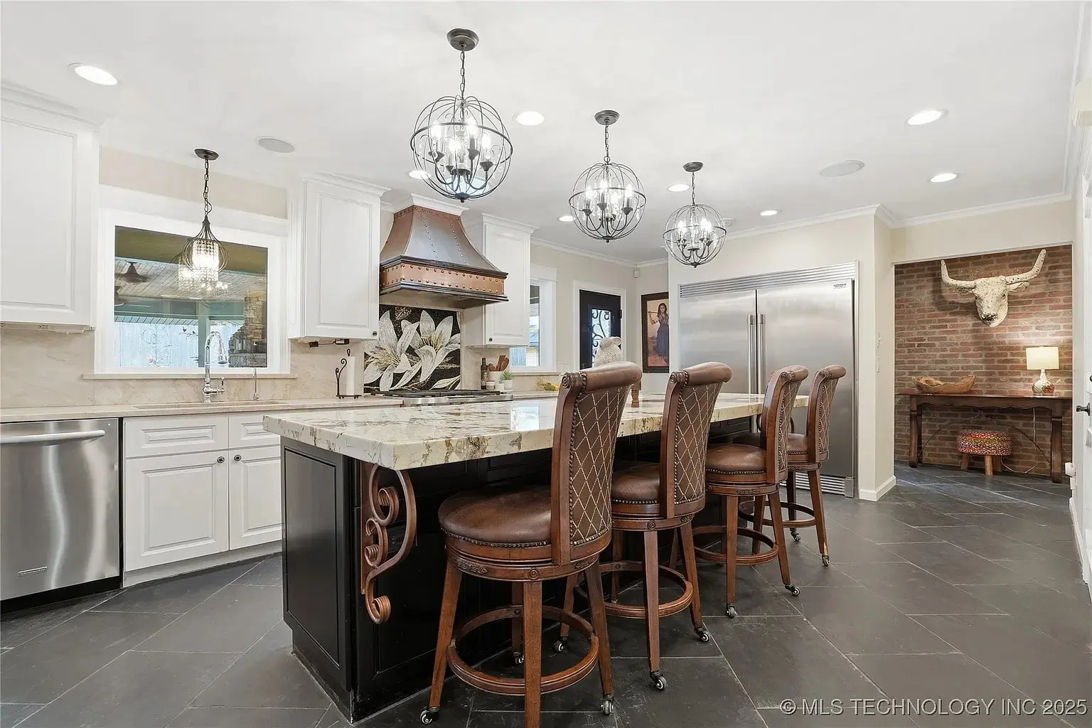 Modern kitchen with large island, bar stools, pendant lights, and stainless steel appliances.