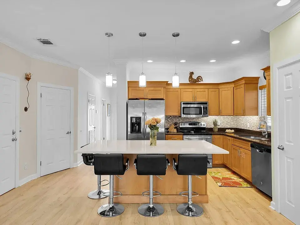Modern kitchen with wooden cabinets, stainless steel appliances, island with bar stools, and pendant lighting.