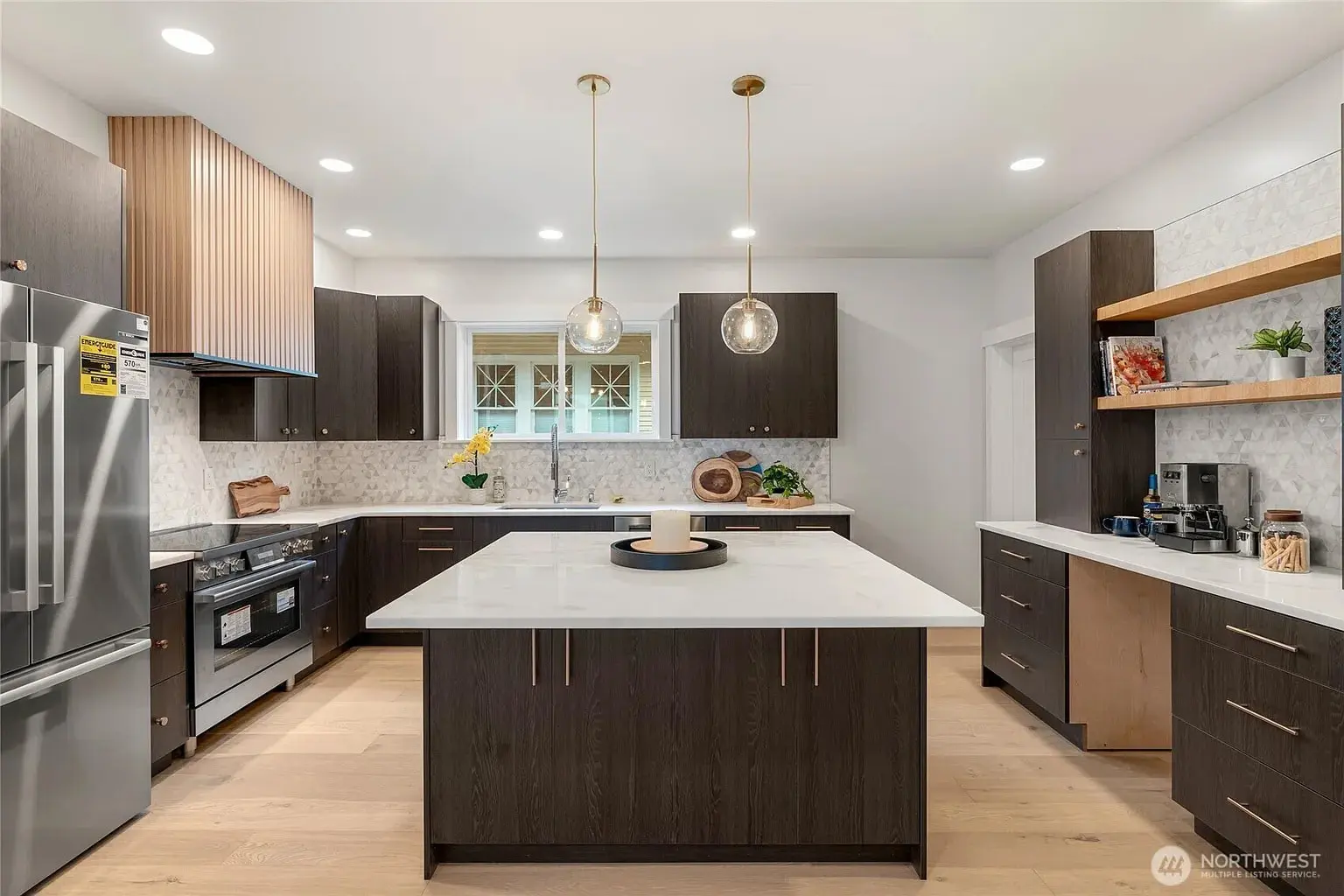 Modern kitchen with dark wood cabinets, large island, stainless steel appliances, and pendant lights.