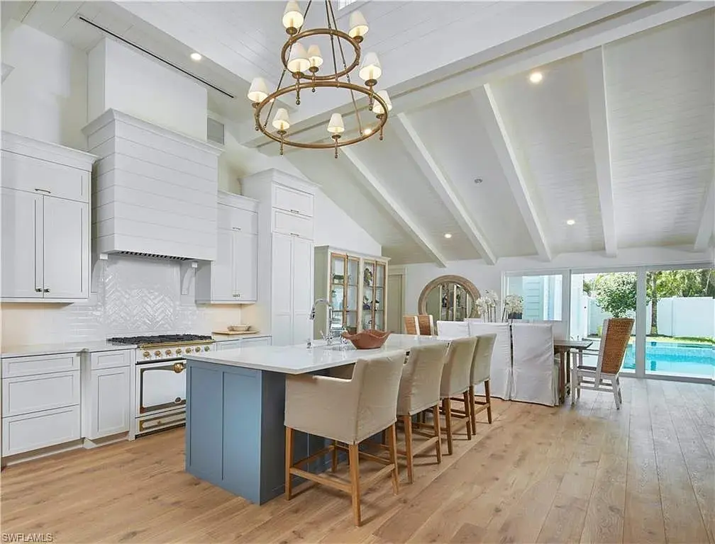 Spacious kitchen with vaulted ceiling, large island, white cabinets, and view of pool through glass doors.