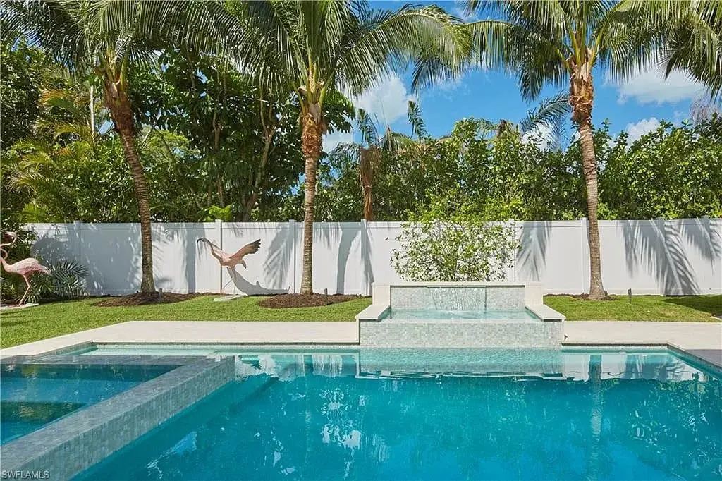 Backyard with a swimming pool, hot tub, palm trees, and a white fence.