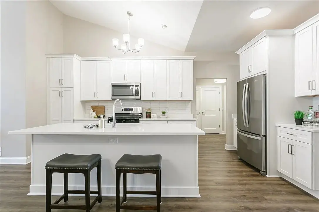 Modern kitchen with white cabinets, stainless steel appliances, and a central island with two stools.