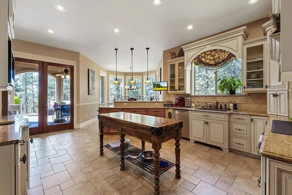 Spacious kitchen with wooden island, cream cabinets, large windows, and doors leading to a patio.