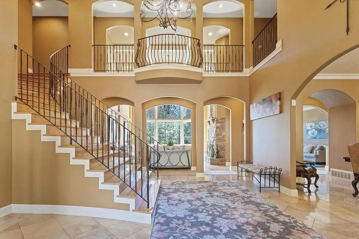 Spacious foyer with grand staircase, chandelier, and arched doorways leading to well-lit rooms.