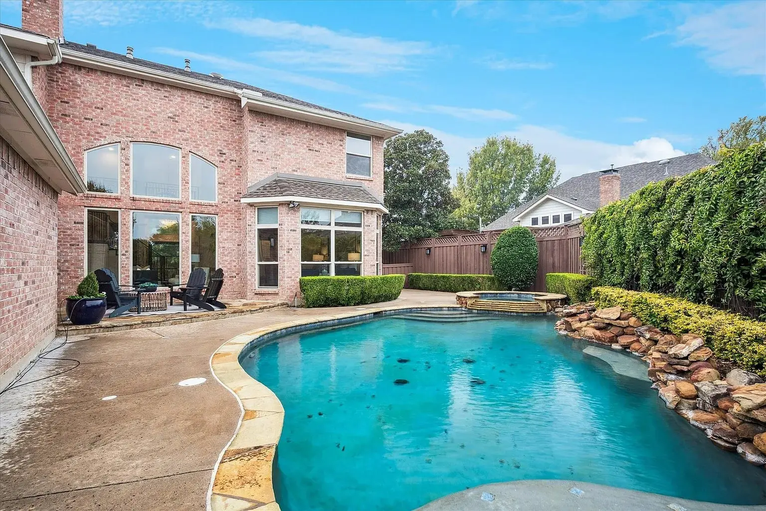 Backyard with a swimming pool, brick house, patio furniture, and landscaped greenery.