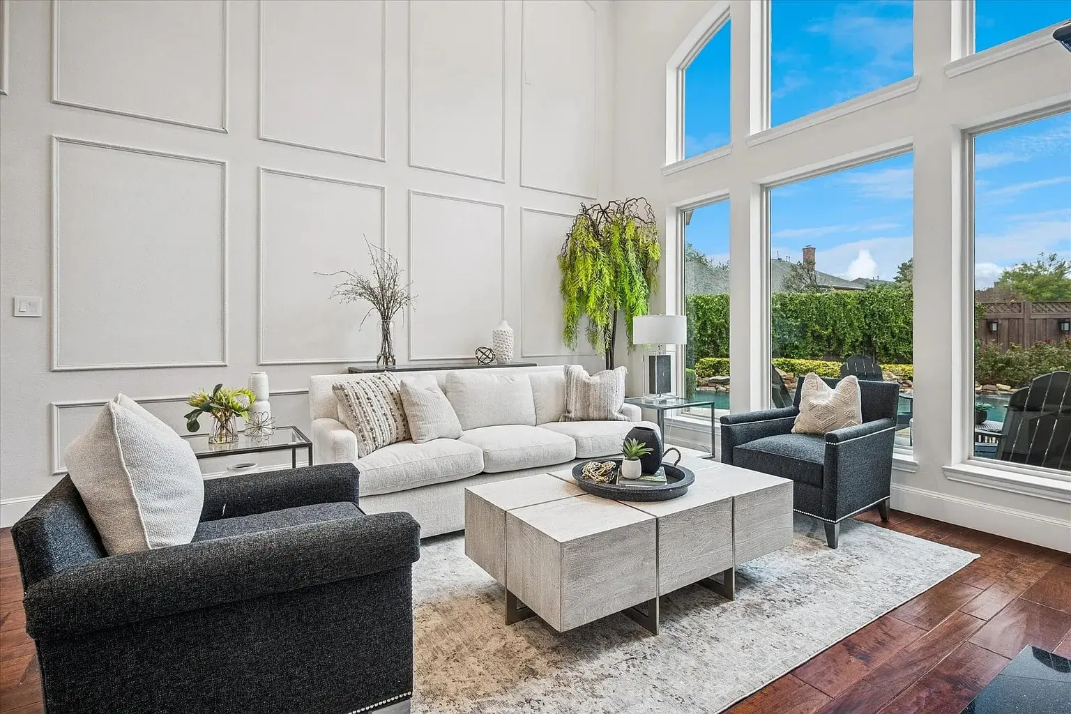 Modern living room with large windows, white walls, dark chairs, and a white sofa.