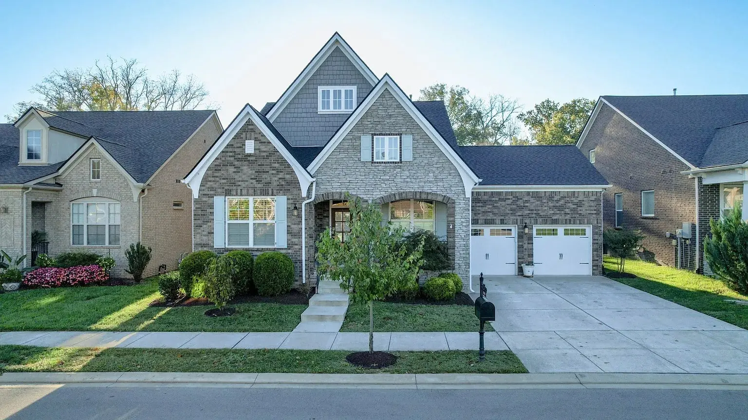 Suburban house with brick facade, gabled roof, two-car garage, and manicured front lawn.