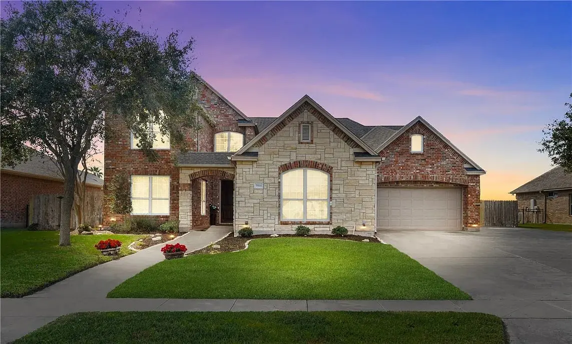 Brick and stone house with a well-maintained lawn and a sunset sky backdrop.