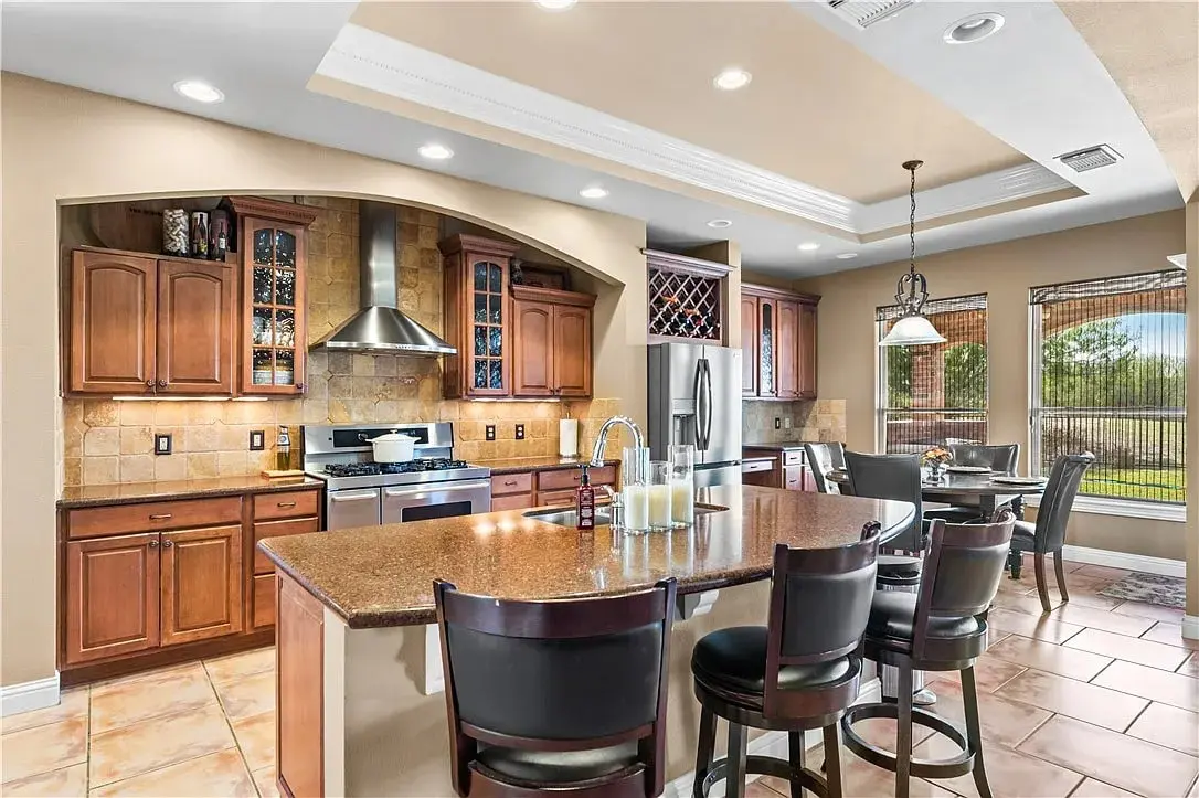 Modern kitchen with wooden cabinets, island with bar stools, stainless steel appliances, and dining area.