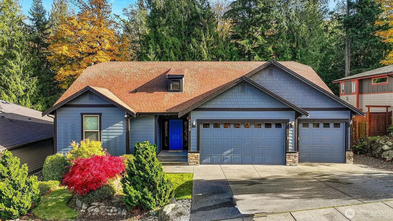 Blue house with a red roof, surrounded by trees, featuring a blue front door and garage.