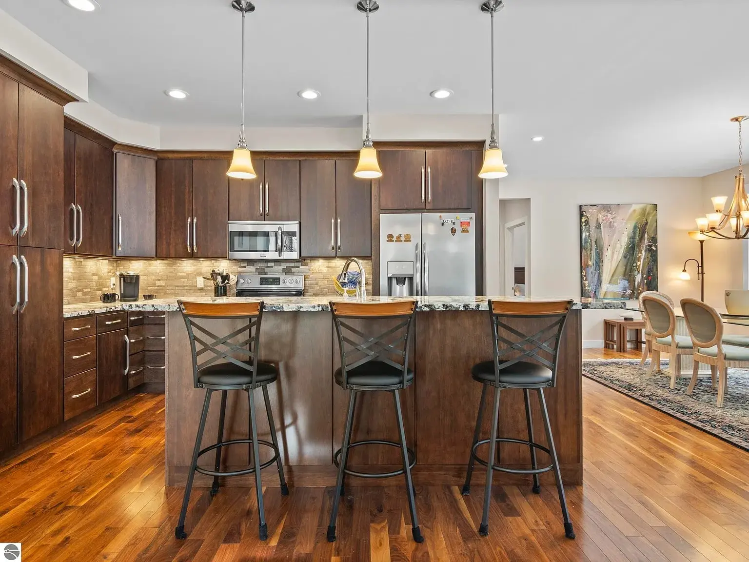 Modern kitchen with dark wood cabinets, granite countertops, and three bar stools at the island.