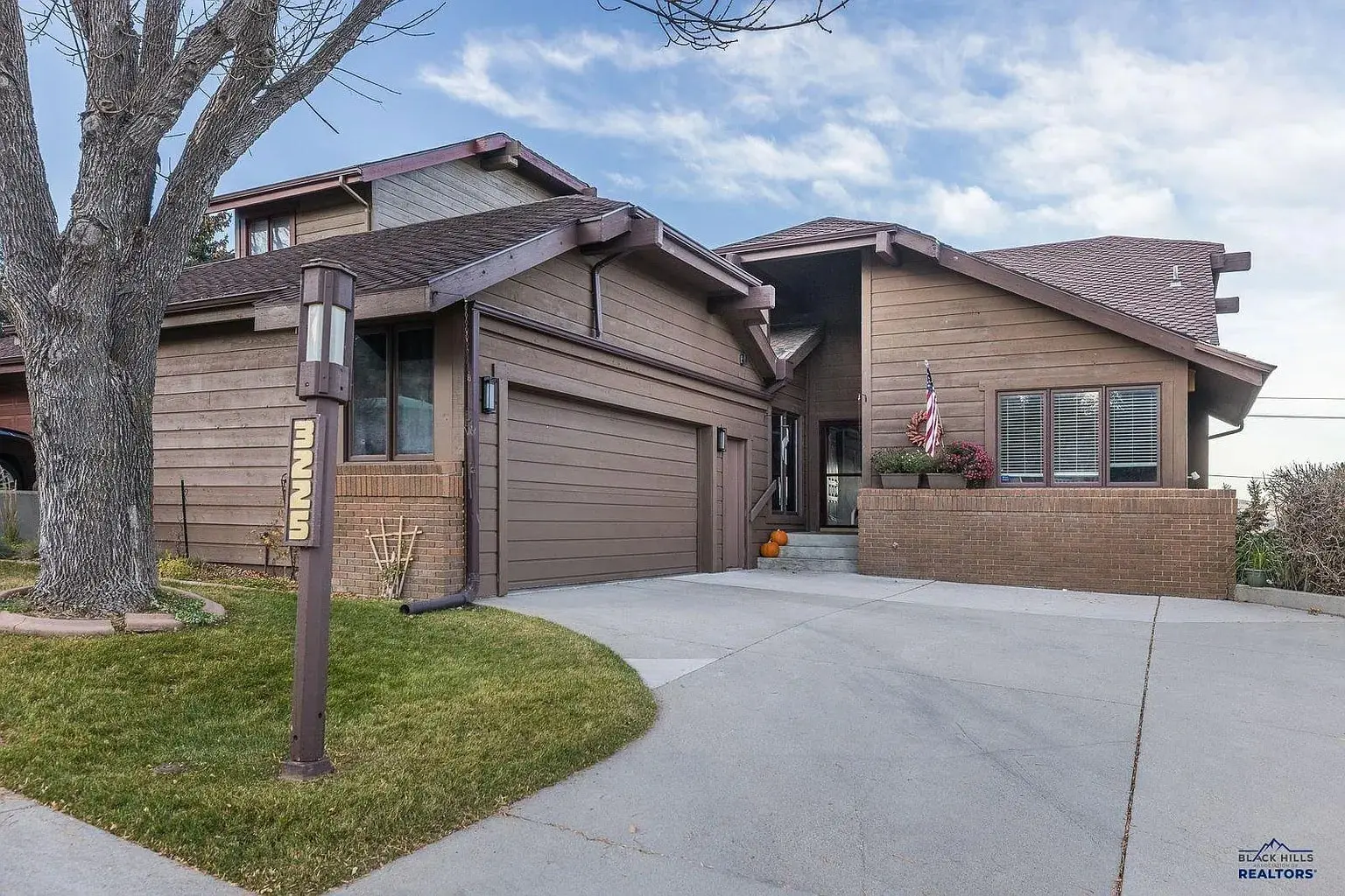 Two-story brown house with a garage, American flag, and a pumpkin on the porch.