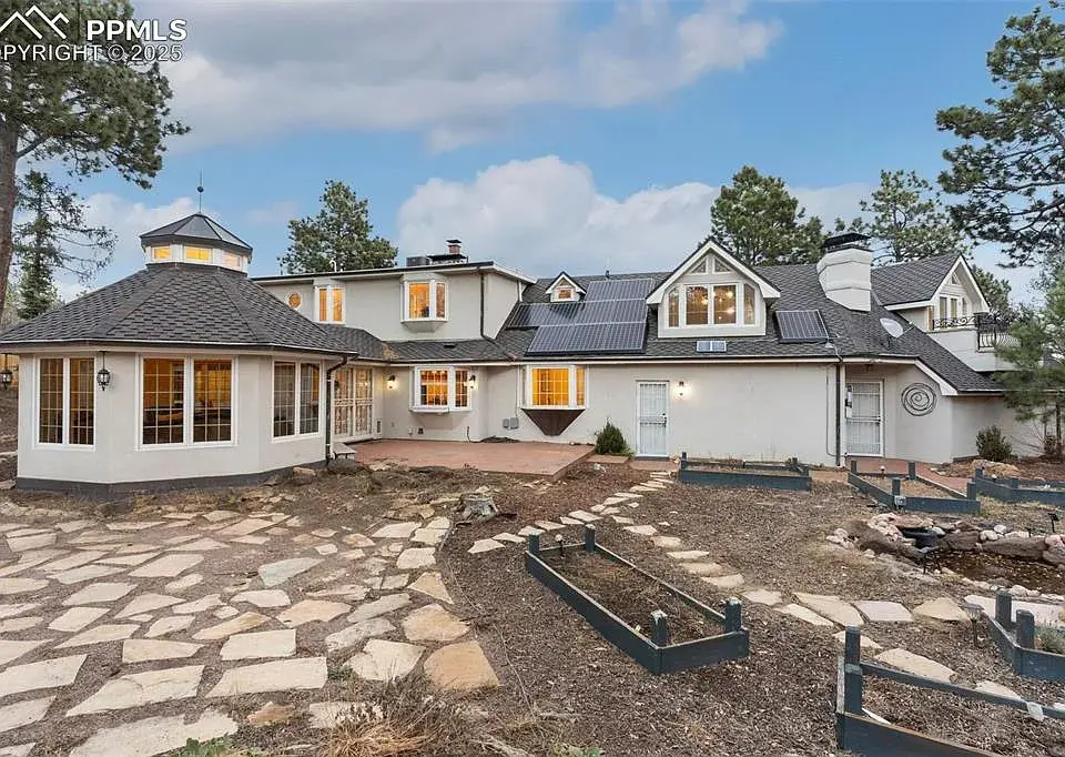 Large, two-story house with multiple gables, surrounded by stone paths and garden beds.