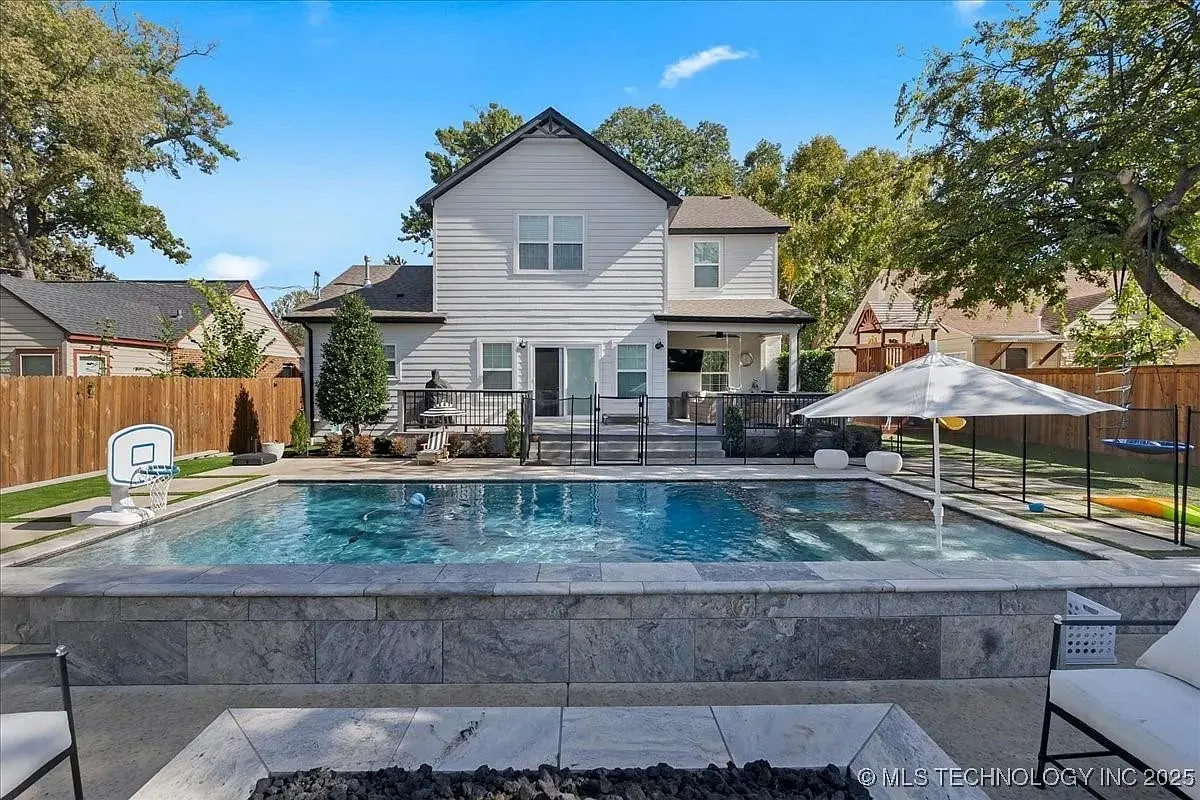 Backyard with a swimming pool, basketball hoop, and patio furniture in front of a two-story house.