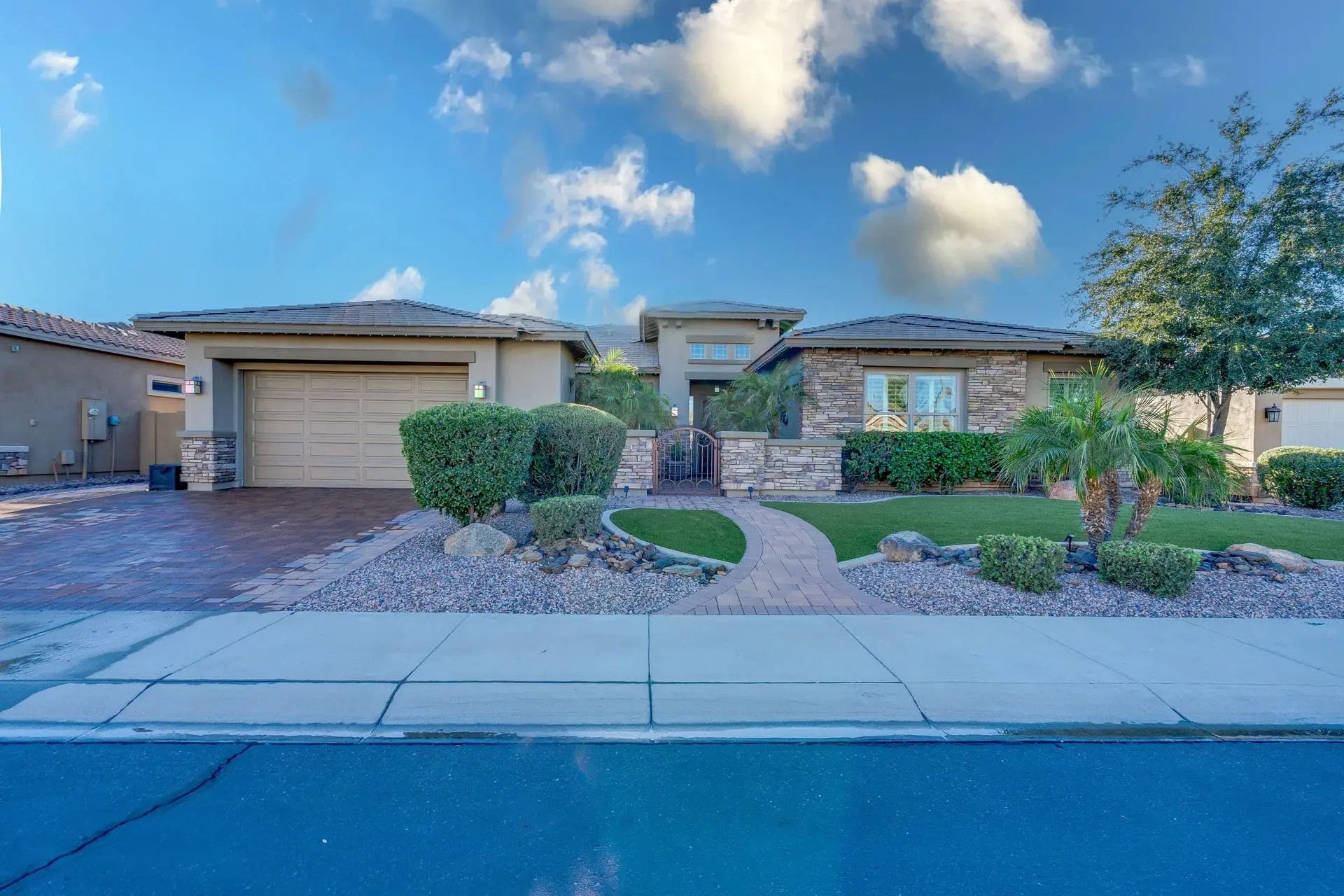 Single-story modern home with stone facade, desert landscaping, gated entry, driveway and two-car garage.